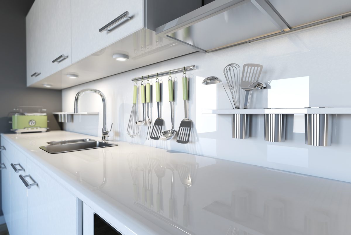 A white kitchen with LED strip lights under the wall cabinets lighting a glossy benchtop and a rail of utensils