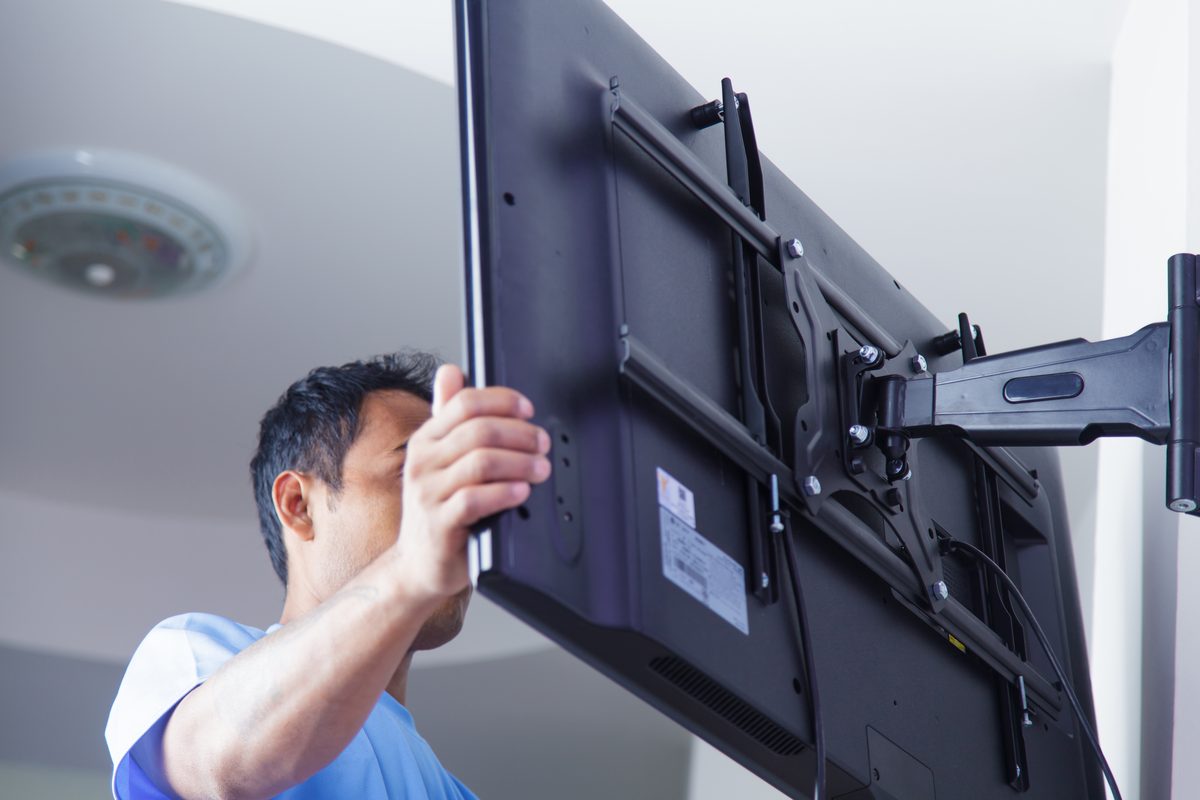 A man lifting a flat screen TV onto a swing-arm bracket fixed to a white wall